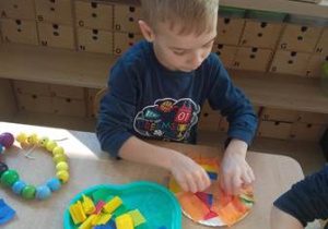 Chłopiec siedzi przy stoliku i układa swoją kompozycję z kawałków kolorowej bibuły