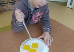 Chłopiec rozprowadza klej za pomocą pędzelka w obrębie papierowego talerzyka