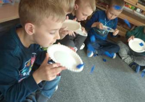Chłopcy wprawiają w ruch kawałki niebieskiej bibuły oddychając nosem