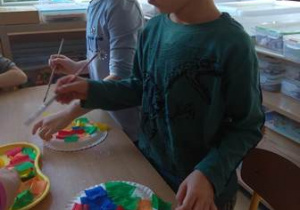 Dziewczynka i chłopiec doklejają kolorowe kawałki bibuły do papierowych talerzyków