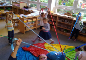 Dzieci biorą udział w zabawie ruchowej "Ośmiornica: Część dzieci unosi taśmy tworząc labirynt, pozostałe dzieci przechodzą przez niego