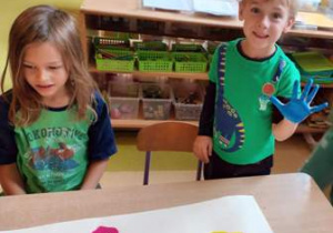 Dwóch chłopców odbija na dużym papierze kształt swoich rąk pomalowanych farbą