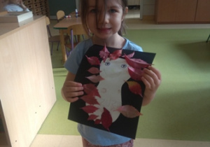 Dziewczynka prezentuje wykonaną pracę przedstawiającą jeża z liści