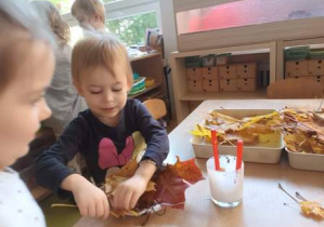 Dziewczynki przyklejają kompozycję z liści i kasztanów na papierowym talerzyku