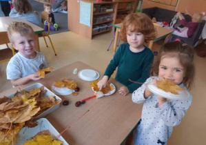 Dzieci przy stoliku wyklejają papierowy talerzyk liśćmi tworząc jesienną kompozycję