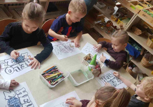 Dzieci siedzą przy stole i kolorują noworoczne rysunki