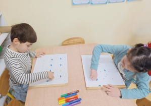 Dzieci przybijają szpilki do kartek ułożonych na korkowych tablicach