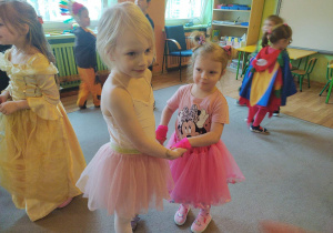 Dwie dziewczynki w strojach karnawałowych tańczą trzymając się za ręce