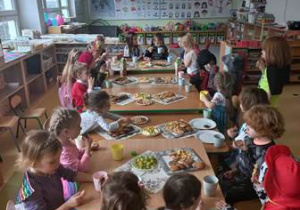 Dzieci siedzą przy stolikach i jedzą poczęstunek zorganizowany z okazji balu karnawałowego