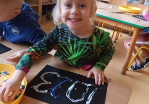 Dziewczynka wykleja napis 2023 rok przy użyciu brokatowej pianki