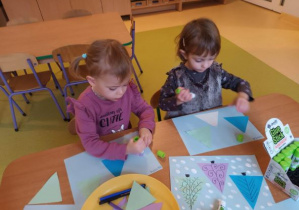 Dziewczynki przyklejają papierowe trójkąty i ozdabiają je na kształt drzewa