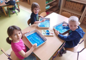 Dzieci malują niebieską farbą tło dla zimowego drzewa
