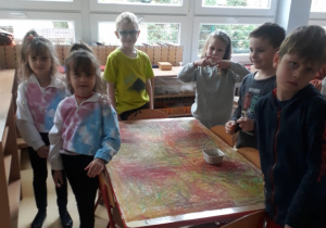 dzieci stoją przy stoliku, na którym leży papier z kreślonymi wcześniej kołami