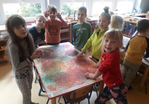 dzieci stoją przy stoliku i prezentują efekt swojej pracy czyli kreślenia kół