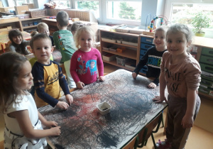 dzieci stoją przy stoliku, na którym leży papier z kreślonymi wcześniej kołami