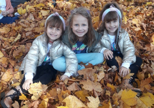 trzy dziewczynki pozują do zdjęcia w stercie liści