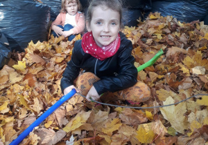dziewczynka z grabiami kuca w stercie liści