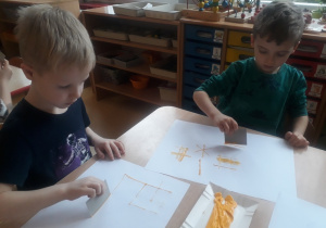 chłopcy odbijają karton umoczony w farbie tworząc kompozycję z linii