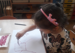 dziewczynka odbija karton umoczony w farbie tworząc kompozycję z linii