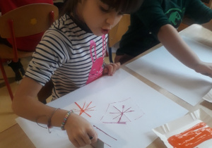 dzieci odbijają karton umoczony w farbie tworząc kompozycję z linii