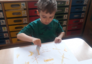 chłopiec odbija karton umoczony w farbie tworząc kompozycję z linii