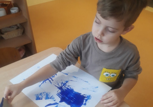 chłopiec odbija karton umoczony w farbie tworząc kompozycję z linii