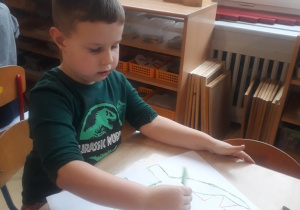 chłopiec odbija karton umoczony w farbie tworząc dinozaura