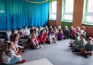 Dzieci siedzą i słuchają bajki czytanej przez studentów