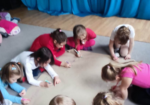 Dzieci siedzą na dywanie i rysują na dużym arkuszu papieru