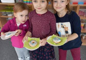 Trzy dziewczynki prezentują swoje wytwory plastyczne - umieszczone na talerzyku pączki uformowane z masy solnej i ozdobione według własnej inwencji twórczej dziewczynek