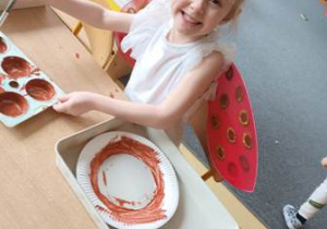 Dziewczynka szykuje baze pod stworzenie pracy plastycznej - maluje farbą talerzyk papierowy