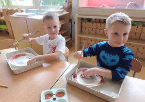 Chłopcy malują brązową farbą papierowe talerzyki z wyciętym środkiem