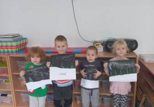 Dzieci stoją i trzymają w dłoniach swoje prace plastyczne przedstawiające zjawisko zorzy polarnej