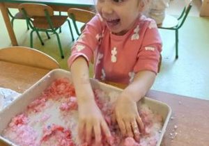 Anielka przy stoku bierze udział w zabawie sensorycznej z zabarwionym sztucznym śniegiem