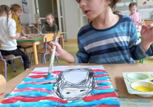 Chłopiec maluje farbami tło dookoła narysowanego przez siebie pingwina