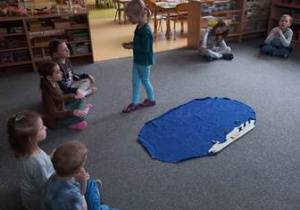 Dzieci siedzą w kręgu na dywanie i pracują z materiałem rozwojowym przybliżającym zagadnienia związane z położeniem Arktyki i Antarktydy na mapie