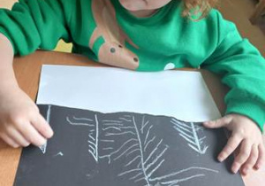 Chłopiec rysuje choinki w czasie wykonywania pracy plastycznej