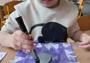 Chłopiec za pomocą mazaka dorysowuje umieszczonej na pracy plastycznej foce uśmiech