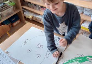 Chłopiec siedzi przy stoliku i rysuje kubistyczny portret