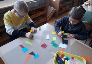 chłopiec i dziewczynka przyklejają figury tworząc abstrakcję geometryczną