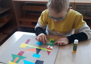 chłopiec przykleja figury tworząc abstrakcję geometryczną