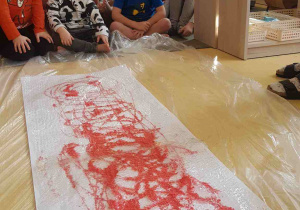Dzieci czekają na przejście boso po folii rozłożonej na papierze z czerwoną farbą
