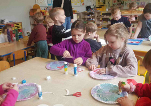 Dzieci drą kawałki papieru i przyklejają do talerzyka