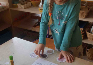 Dziewczynka zastanawia się jak uporządkować kolorowe pączki z papieru na karcie pracy