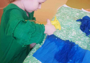 Dziewczynka przygotowuje tło pracy plastycznej, mocząc niebieską bibułę