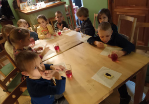 Dzieci siedzą przy stole i częstują się ciasteczkami oraz pysznym sokiem