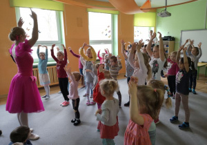 Tancerka ubrana w różową sukienkę pokazuje dziewczynkom ruch