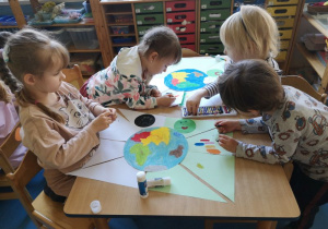 Dzieci siedzą przy stoliku i przygotowują swoje plakaty na Dzień Ziemi