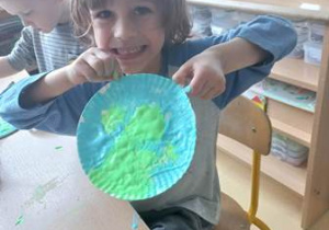 Chłopiec trzyma w dłoniach talerzyk papierowy pomalowany rosnąca farbą w kolorach Ziemi