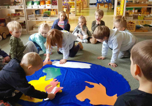 Dzieci układają kontynenty na niebieskiej płachcie